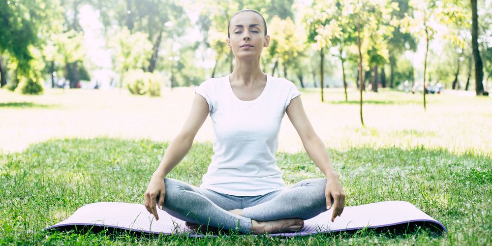 Eine Frau macht Yoga in der Natur, um Kopfschmerzen aufgrund von Stress vorbeugend zu behandeln.