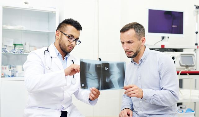 Ein Arzt zeigt einem Patienten mögliche Behandlungsmethoden beim Bänderriss. 