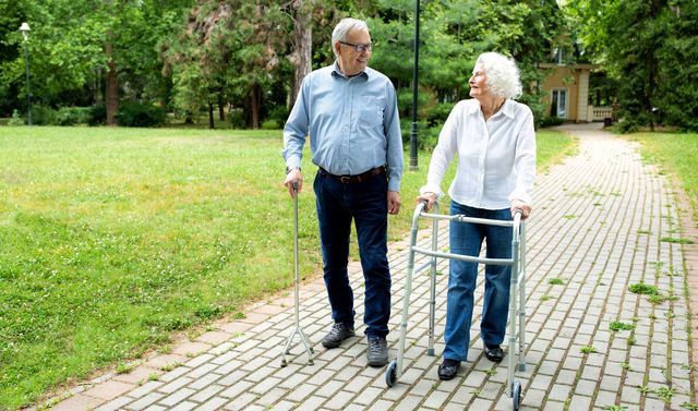 Eine ältere Frau mit Spinalkanalstenose geht mit ihrem Mann und einer leicht gebeugten Haltung spazieren.