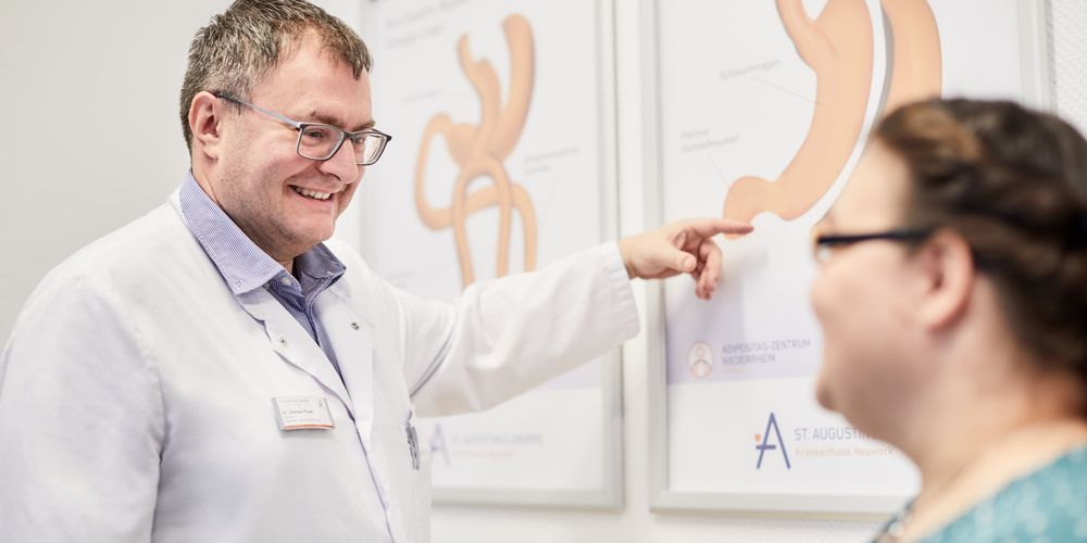 Ein Arzt erklärt einer Patientin anhand eines Schaubildes des Magens, warum eine Adipositas-Behandlung wichtig ist.