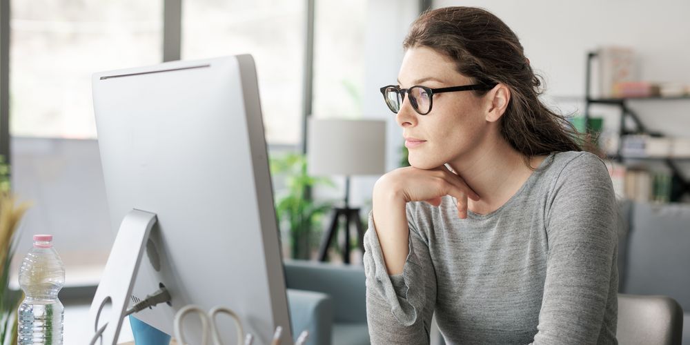 Eine sitzende Frau vorm Computer steht für wenig Bewegung als Ursache für Rückenschmerzen.