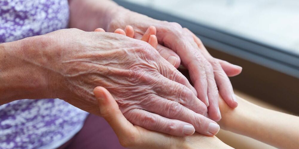 Zwei junge Hände halten zwei weitere Hände, einer älteren Person in der Hand. 